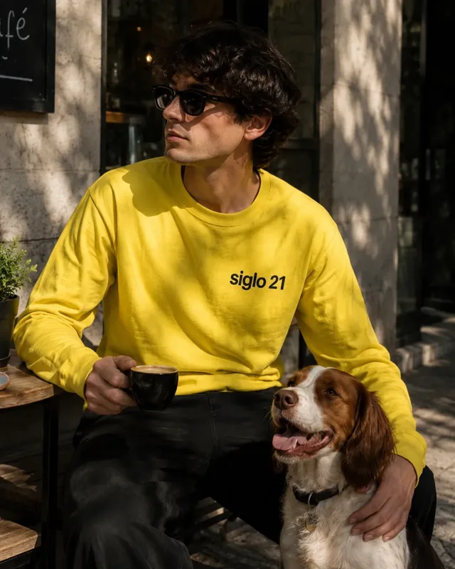 Modelo con sudadera amarilla democracia21 con el mensaje "siglo 21" en el pecho, sentado con su perro en una terraza